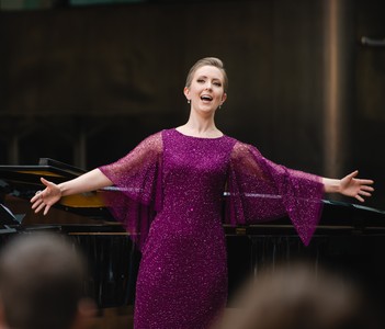 Arms outstretched, Sarah sings in a purple sequined dress in the bough of a piano